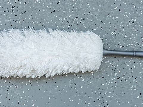 Soft white cobweb duster brush with plastic handle on a grey surface